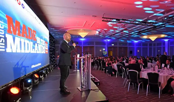 PJ Ellis, Host, speaking on stage at the Made in the Midlands Awards 2025 in Birmingham, with the event logo displayed on screen and guests seated at gala tables.