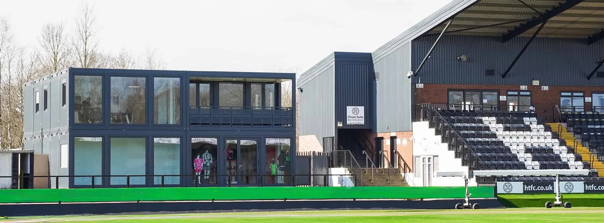 Modular hospitality and retail suite at Hednesford FC football ground, built from stacked container units beside the main stadium seating.