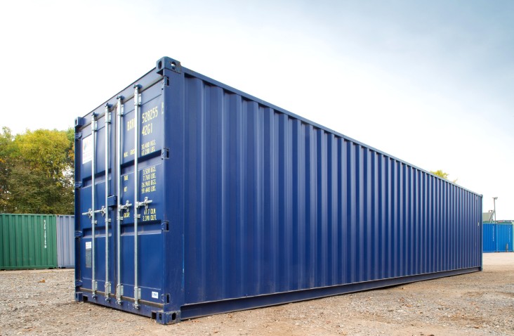 Blue 40ft shipping container with closed double doors and long corrugated steel side, photographed on a yard with other containers in the background.