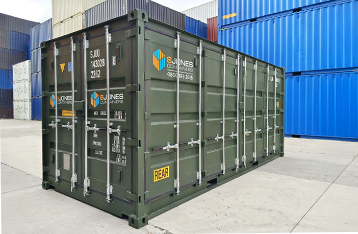 Green 20ft side opening shipping container with double cargo doors and full-length side access, branded with S Jones Containers logo, positioned in a storage yard with stacked blue containers in the background