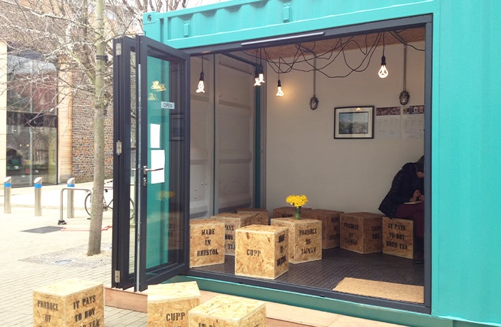 Colourful converted shipping container kiosk with exterior serving hatch and internal feature lighting. 