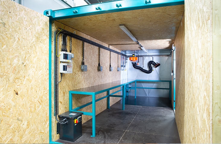 Interior of an insulated shipping container workshop with OSB lining, steel workbench, electrical fittings and fume extraction system. 