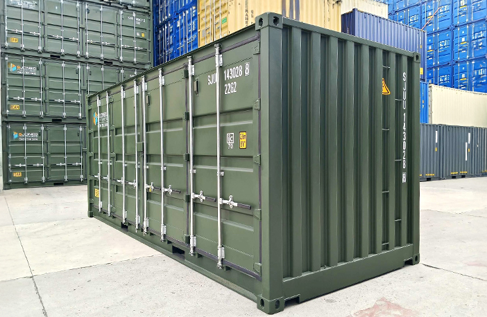 Green 20ft side opening shipping container with side doors closed, shown in a container yard with stacked shipping containers in the background