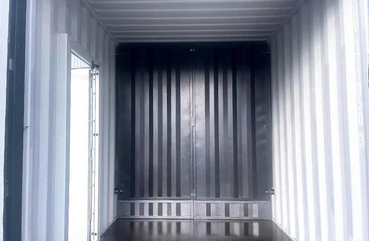 Interior of a high cube shipping container with a removable black steel bulkhead partition secured in place, showing extra vertical space and white internal wall lining. 