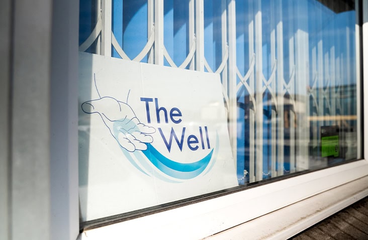 Close-up view of a window displaying a sign for The Well food bank charity, showing a hand graphic with blue waves.