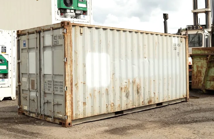 Used 20ft shipping container in light grey with visible rust patches and surface wear, closed cargo doors, and weathered exterior, suitable for secure storage or site use. 