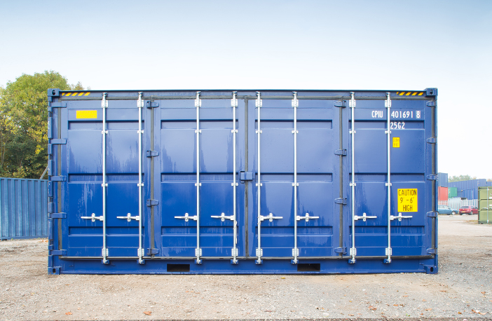     Front view of a blue 40ft high cube side opening shipping container with all side doors closed, positioned on a gravel surface in a storage yard with other containers in the background. 