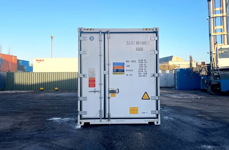 Front view of a 40ft white refrigerated container, showing closed double doors with load capacity details and warning labels, positioned outdoors on a yard surface. 
