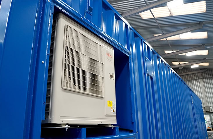 Fujitsu HVAC condenser unit installed within a recessed cut-out on the side wall of a blue shipping container. 