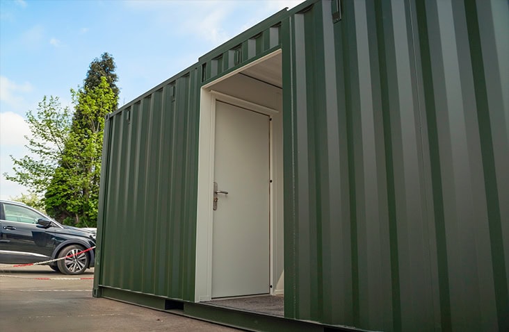 Green topper container featuring a white personnel door, photographed from a low angle in an outdoor yard. 