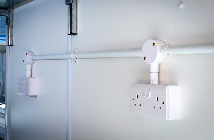Double 13A UK mains power sockets installed on surface-mounted conduit inside a converted shipping container. 