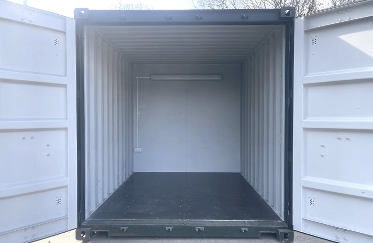 Interior of a converted shipping container showing a clean finished workspace with lighting and electrics fitted to a partition. 