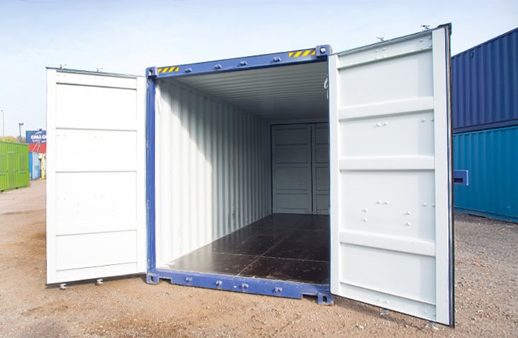 A blue 20ft high cube tunnel shipping container with both front end doors open, showing the clean, empty interior and dark plywood flooring on a gravel surface with other containers in the background. 