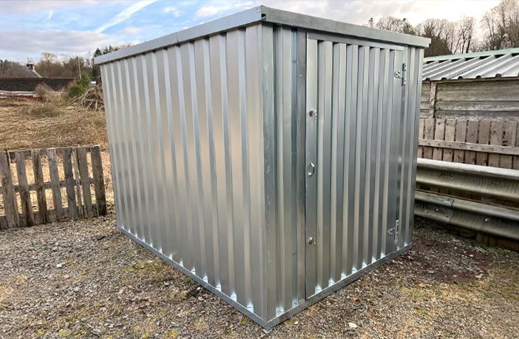 Galvanised flat pack steel storage unit with single door, installed on a farmyard for secure outdoor storage.