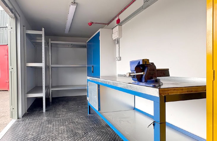 Shipping container workshop with industrial workbench and vice, storage shelving units, and a yellow tool locker, designed for onsite engineering use. 