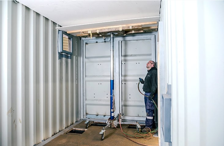 An engineer working inside a shipping container during lining and insulation preparation, using lifting equipment to support the internal roof panel. 