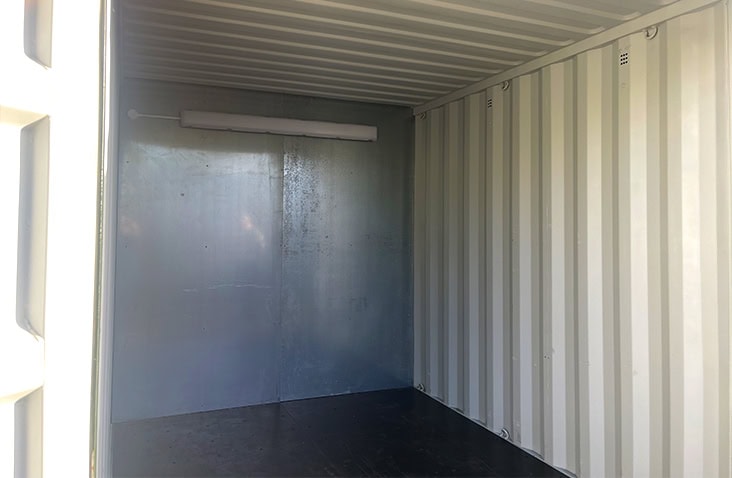 Inside view of a shipping container with a steel partition wall and overhead light installed. 