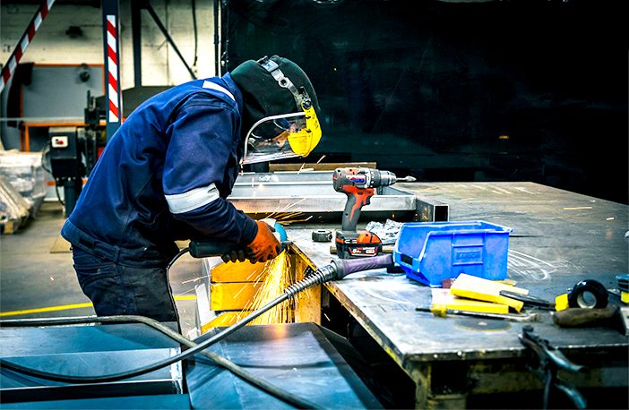 An engineer working in the S Jones Containers workshop, using power tools to modify and fabricate a bespoke shipping container conversion