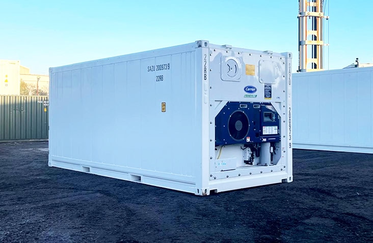 Angled rear-side view of a 20ft white refrigerated shipping container, showing the exposed refrigeration machinery unit at one end and smooth exterior panel walls, positioned outdoors on a container yard surface. 