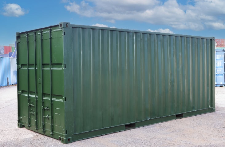     Refurbished 20ft shipping container painted dark green, shown with closed cargo doors on a yard surface, with other containers and blue sky in the background. 