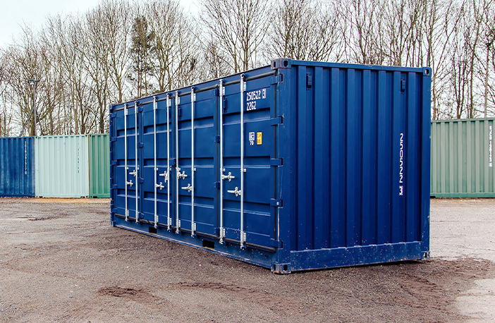 Blue 20ft side opening shipping container with side doors closed, positioned on a gravel surface in a container yard with stacked and lined containers in the background