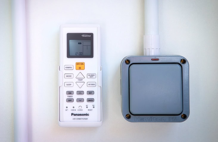 Close-up of Panasonic air conditioning remote control next to an IP66 electrical switch inside a container. 