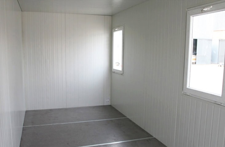 Interior of a flat pack office unit with insulated white panel walls, windows for natural light, and a durable flooring finish