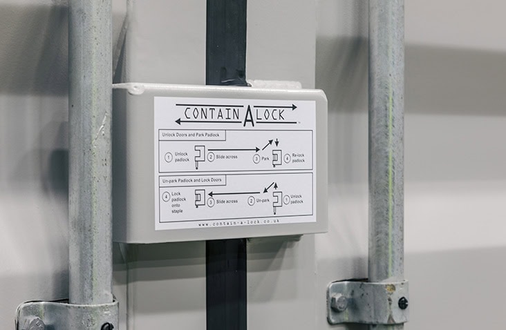 Secure locking system on a shipping container door showing a Contain-A-Lock unit with illustrated instructions for unlocking and locking using a padlock. 