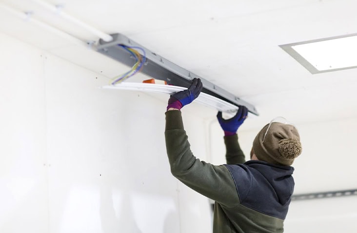 Electrician installing LED lighting into the ceiling of an insulated shipping container interior. 