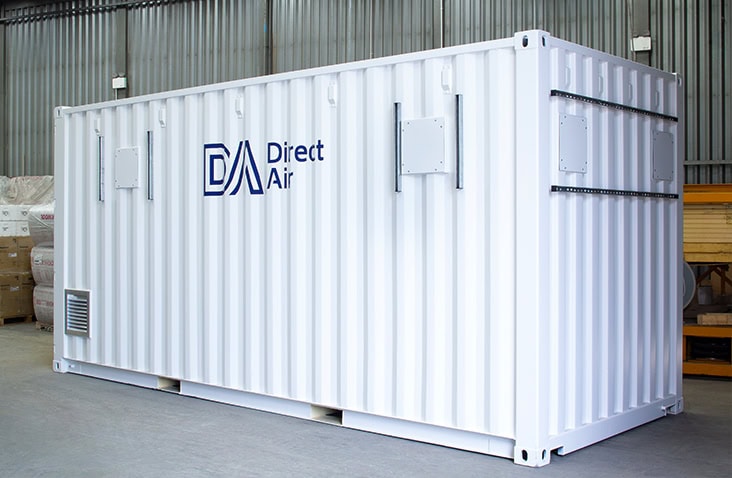 White 20ft shipping container with ‘Direct Air’ branding, placed inside an industrial warehouse with corrugated metal walls and concrete flooring.