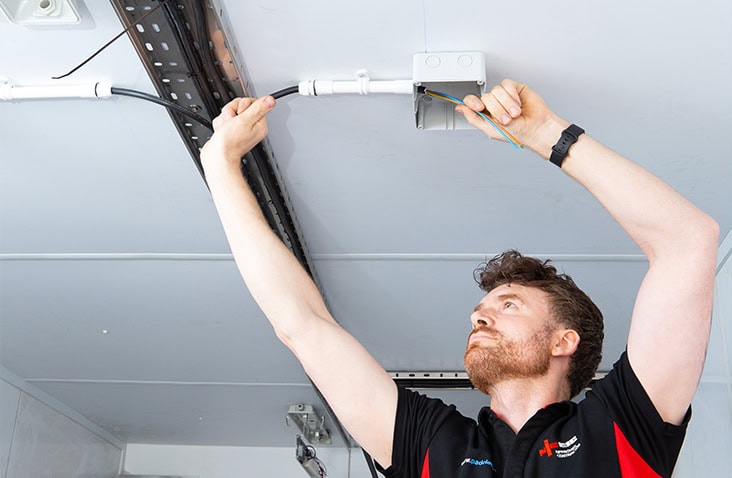 Electrician installing overhead electrical wiring and conduit inside a converted shipping container.