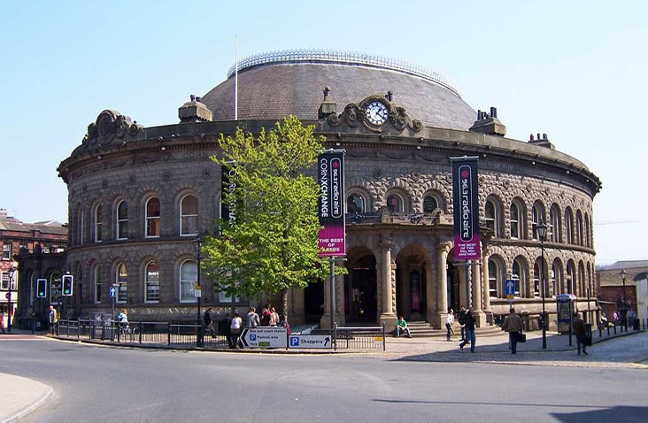The Leeds Corn Exchange historic building with people walking outside, set against a clear sky in Leeds city centre.