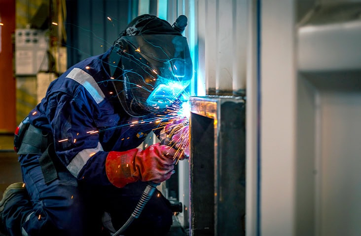 Close-up of an engineer welding steel during a shipping container modification, creating sparks inside a workshop.