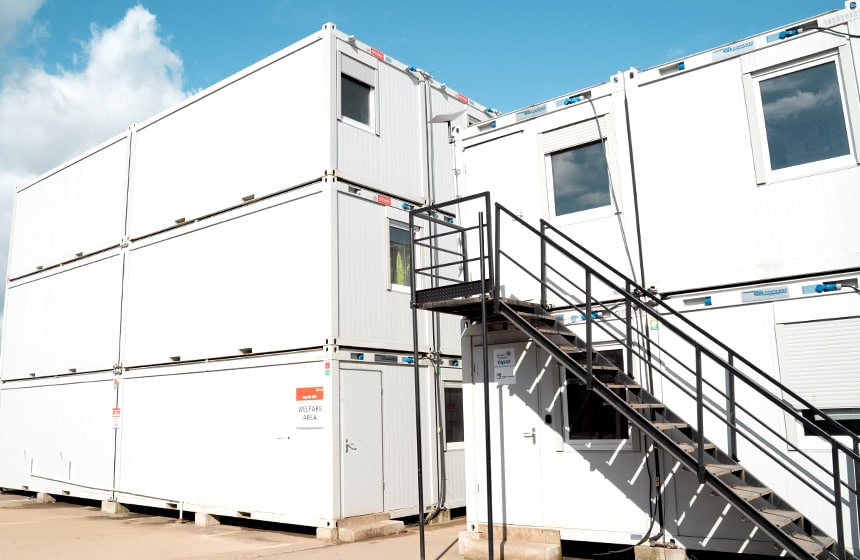 Three-storey modular welfare building with external metal staircase and stacked white units on a construction site designed for Acciona by S Jones Modular Buildings. 