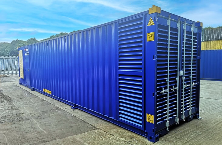 Blue containerised switchgear enclosure with large louvred ventilation panels on the cargo doors and a personnel access door on the side, positioned on a concrete yard.
