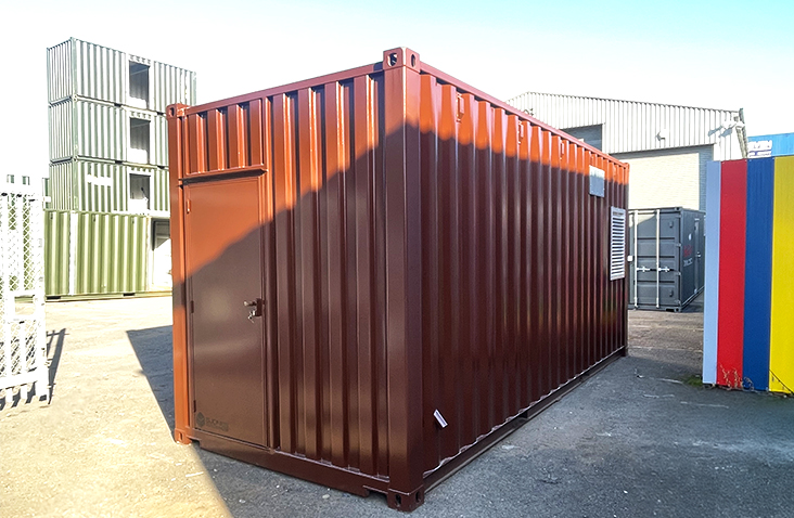 Exterior view of a containerised boiler housing, finished in brown with a personnel access door and ventilation louvre, situated in an industrial yard.