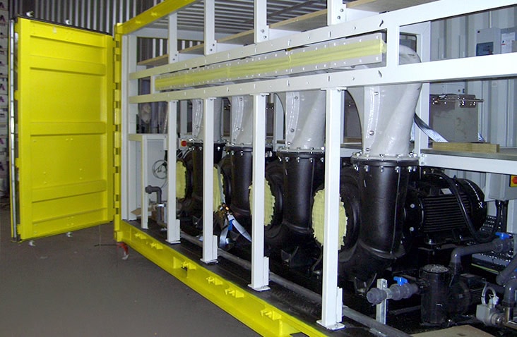 Interior of a yellow containerised water treatment unit housing multiple large industrial pumps, pipework, and support framework, visible through opened side doors.