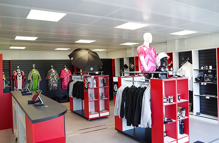 Interior of a modular retail unit featuring clothing displays, sports merchandise, mannequins, and counter space with digital tablets, styled in red, black, and white.