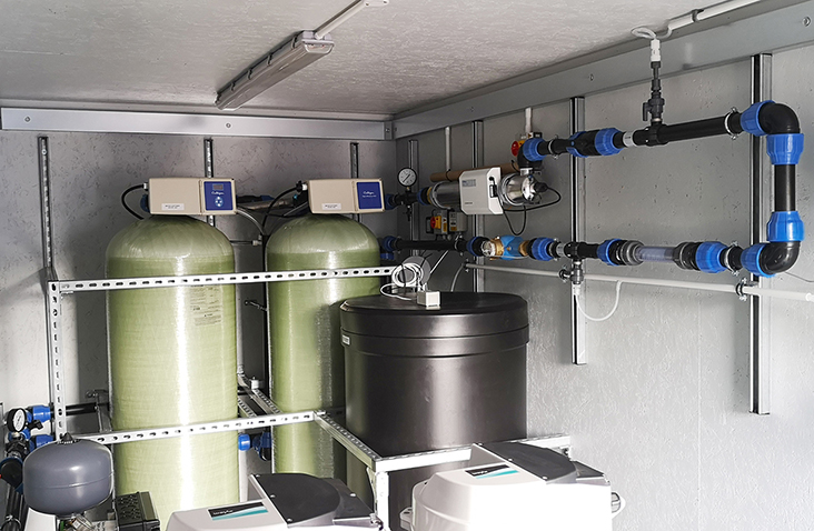Interior of a containerised water treatment system showing twin pressure vessels, control units, and connected pipework mounted on a steel support framework.