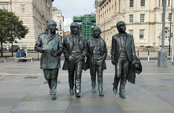 Bronze statues of The Beatles at Pier Head in Liverpool city centre, with historic waterfront buildings in the background on a clear day.