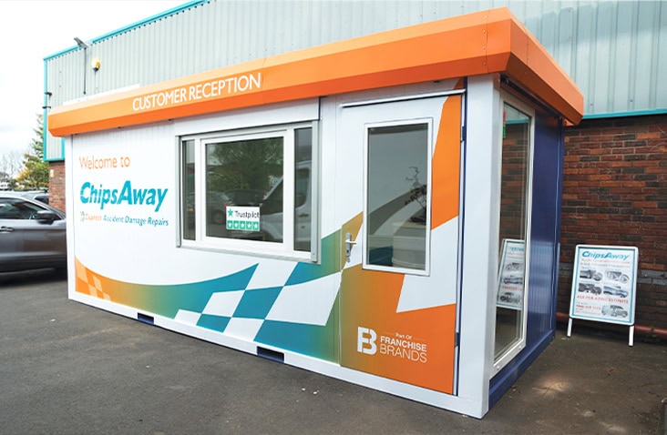 Modular customer reception unit for ChipsAway with orange and blue branding, featuring a door, window, and signage for car repair services.