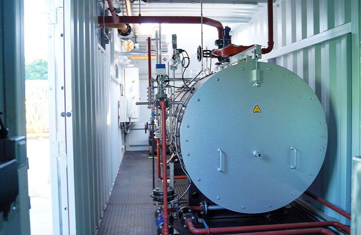 Interior of a containerised steam boiler system, showing the boiler unit, pipework, valves and controls installed by S Jones Conversions 