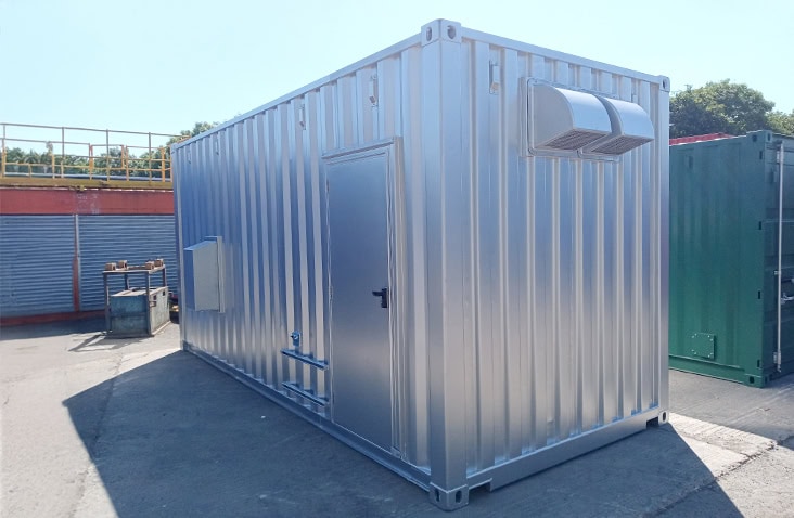 Silver converted switchgear enclosure with a personnel access door, external ventilation louvres, and mounted service connections, positioned in an industrial yard
