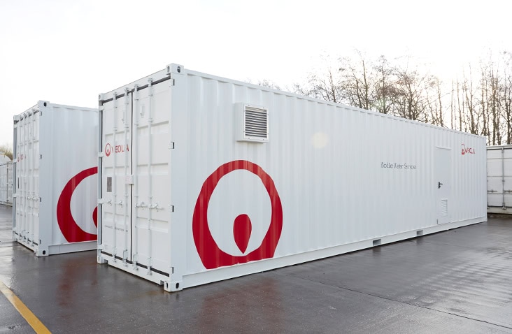 Two white containerised water treatment units branded with the Veolia logo, positioned on a concrete yard. The long side features ventilation louvres and a personnel access door.