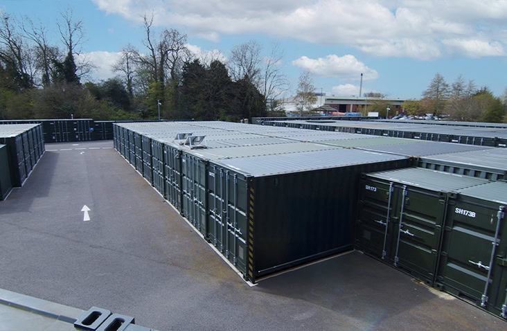 A large outdoor self storage facility with rows of 20ft steel containers arranged in drive-up lanes, viewed from above. 