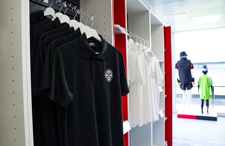 Interior of a modular retail unit displaying branded black and white polo shirts on open shelving.