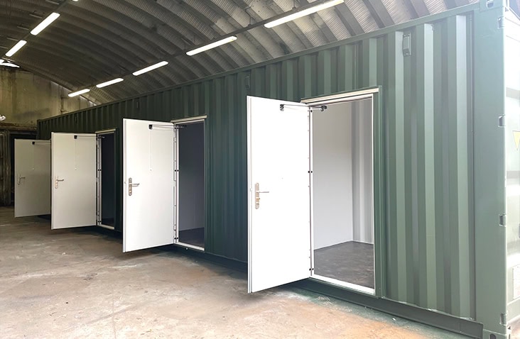 Green multi-store storage container inside a paint booth, with all personnel doors open to show individual internal units. 