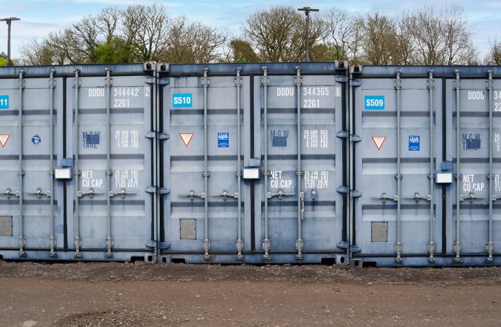Row of blue shipping containers with visibly faded and weathered paint before undergoing restoration