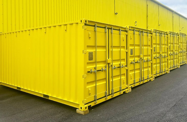 A row of bright yellow 20ft shipping containers positioned side by side on a tarmac self storage site. 