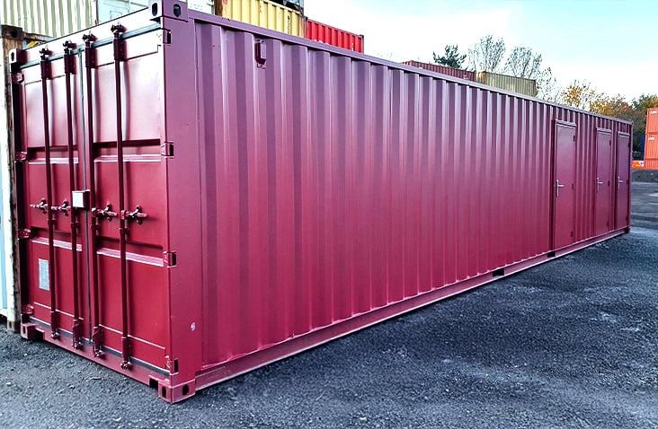 Long burgundy multi-store shipping container with multiple personnel doors along the side, positioned outdoors in a storage yard. 